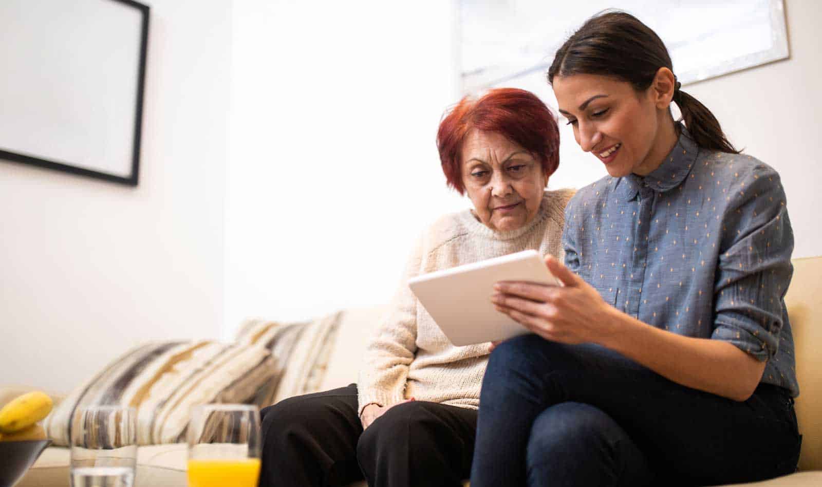 young woman and senior relative looking at a tablet device on the couch together